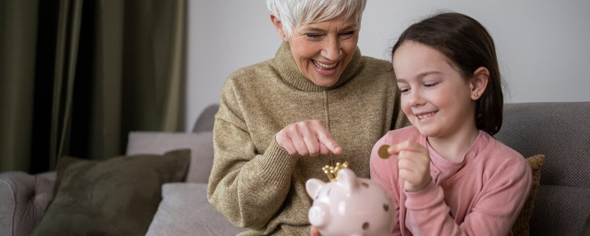 Grand-mère avec une petite fille heureuse mettant une pièce d’argent dans une tirelire. 